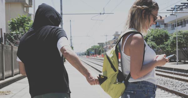 Zakkenroller pakt portemonnee uit rugzak van een vrouw die staat te wachten op de trein.