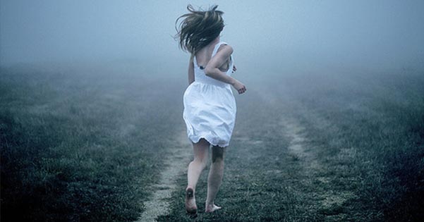 Jonge vrouw in een wit zomerjurkje rent over een mistig grasland