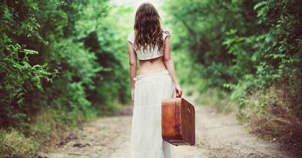 Achteraanzicht van een jonge vrouw met koffer op een bospaadje